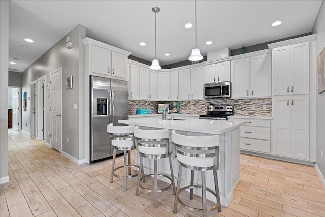 kitchen with white cabinetry, stainless steel appliances, a kitchen breakfast bar, an island with sink, and decorative light fixtures