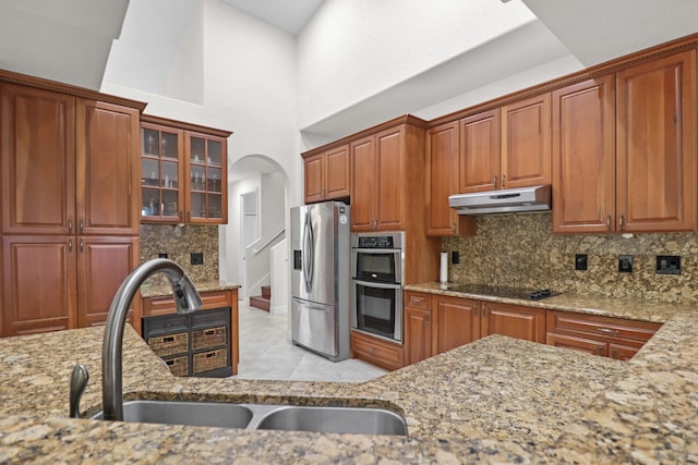 kitchen featuring light stone countertops, sink, a towering ceiling, and stainless steel appliances