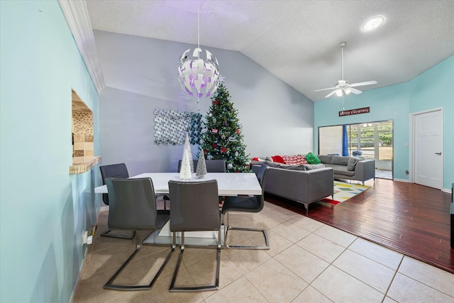 dining space featuring ceiling fan with notable chandelier, lofted ceiling, a textured ceiling, and light tile patterned floors