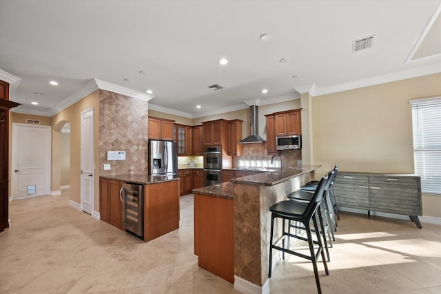 kitchen with wall chimney range hood, a breakfast bar area, stainless steel appliances, wine cooler, and kitchen peninsula