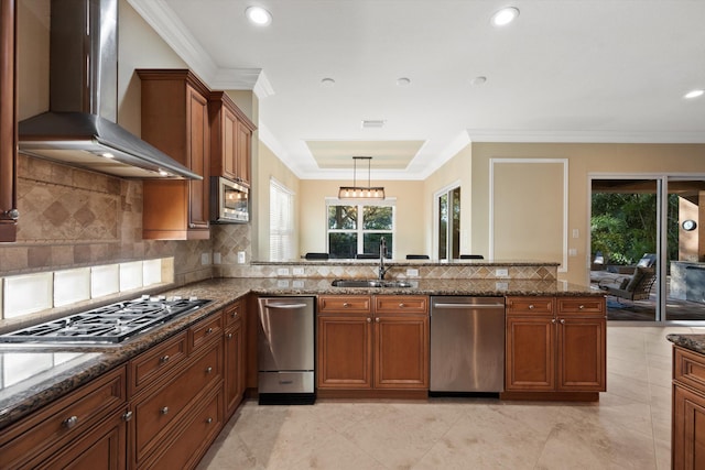 kitchen featuring wall chimney exhaust hood, sink, decorative light fixtures, appliances with stainless steel finishes, and dark stone counters