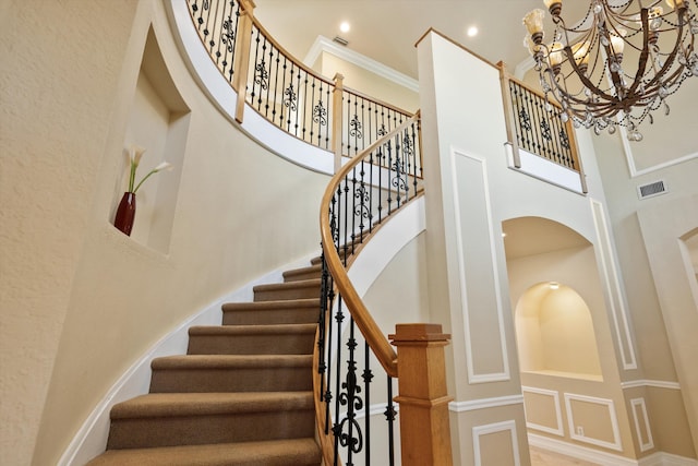 stairway with a high ceiling, ornamental molding, and a notable chandelier