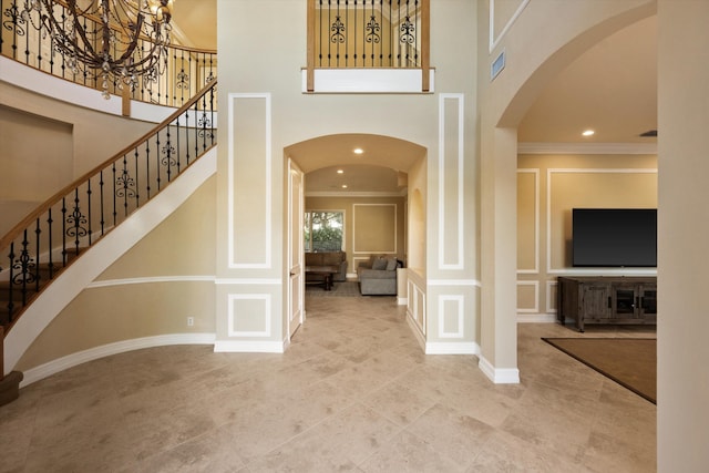 entryway with crown molding, a chandelier, and a high ceiling