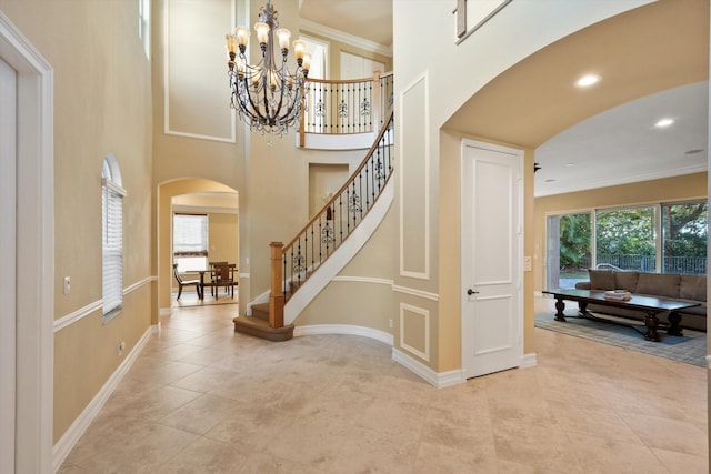 tiled foyer featuring an inviting chandelier, a towering ceiling, and ornamental molding