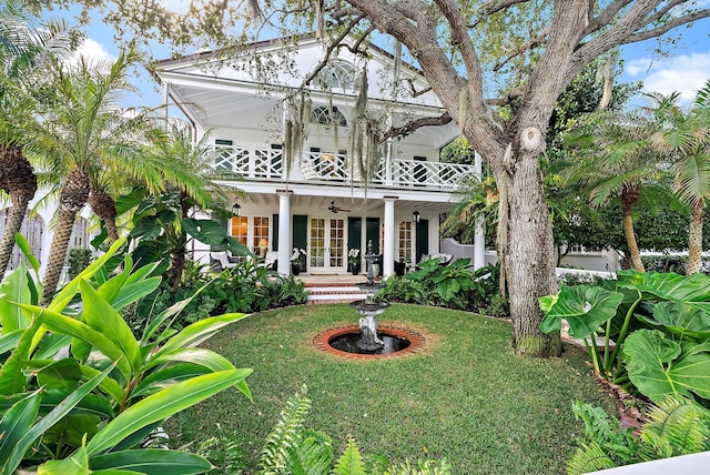 view of front facade with ceiling fan, a balcony, a front yard, and french doors