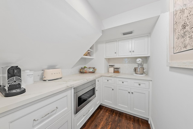 kitchen with stainless steel microwave, tasteful backsplash, light stone counters, dark hardwood / wood-style flooring, and white cabinets