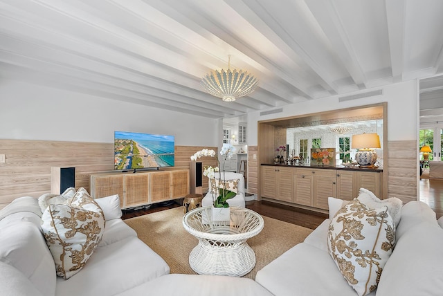 living room featuring beamed ceiling, an inviting chandelier, dark wood-type flooring, and wood walls