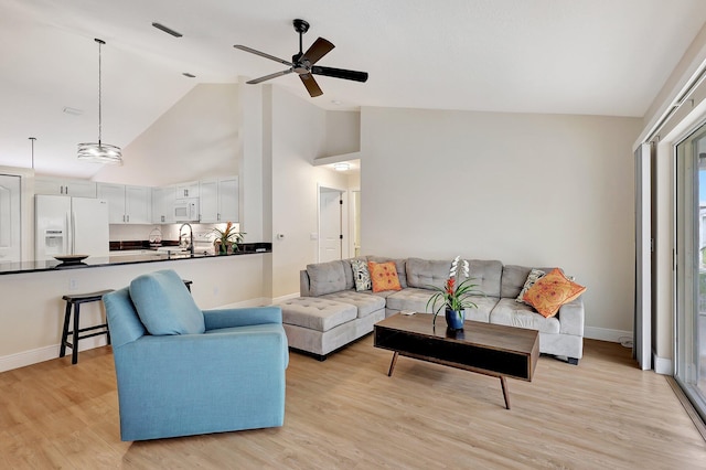 living area featuring high vaulted ceiling, a ceiling fan, light wood-style flooring, and baseboards