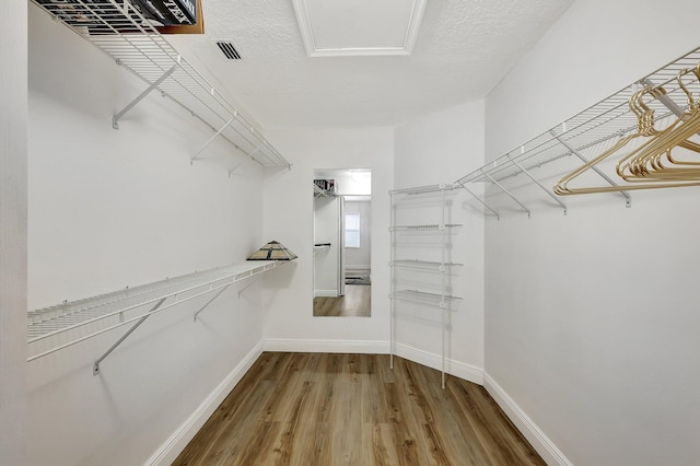 walk in closet with attic access, visible vents, and wood finished floors