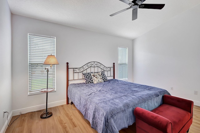 bedroom featuring lofted ceiling, ceiling fan, a textured ceiling, wood finished floors, and baseboards