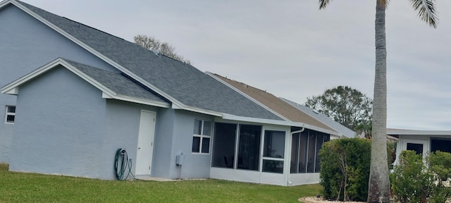 rear view of house featuring a sunroom, a shingled roof, a yard, and stucco siding