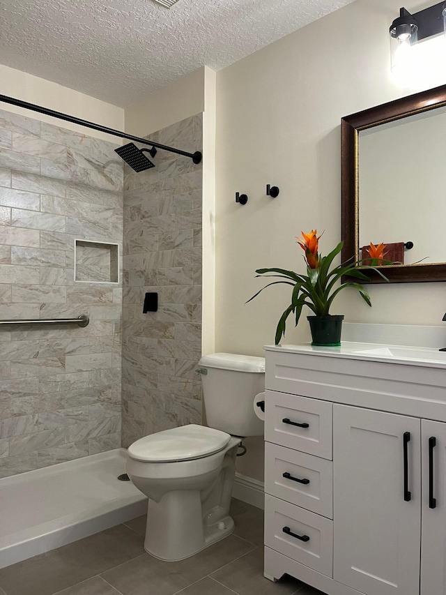 full bathroom with toilet, a tile shower, vanity, a textured ceiling, and tile patterned flooring