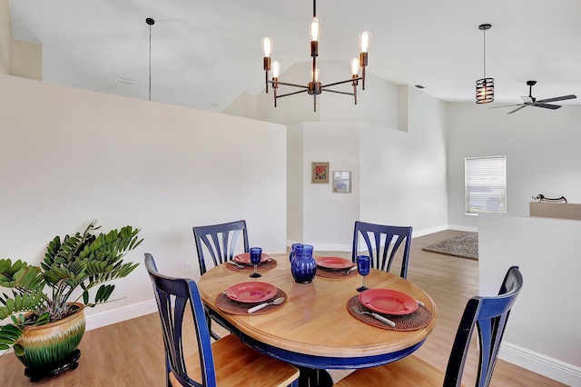 dining space featuring baseboards, ceiling fan with notable chandelier, lofted ceiling, and light wood-style floors