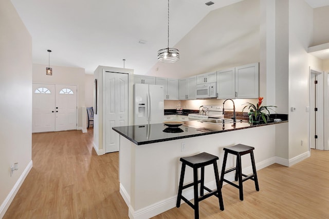 kitchen featuring decorative light fixtures, a sink, high vaulted ceiling, white appliances, and a peninsula