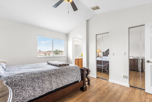 bedroom featuring vaulted ceiling, ceiling fan, light hardwood / wood-style flooring, and two closets