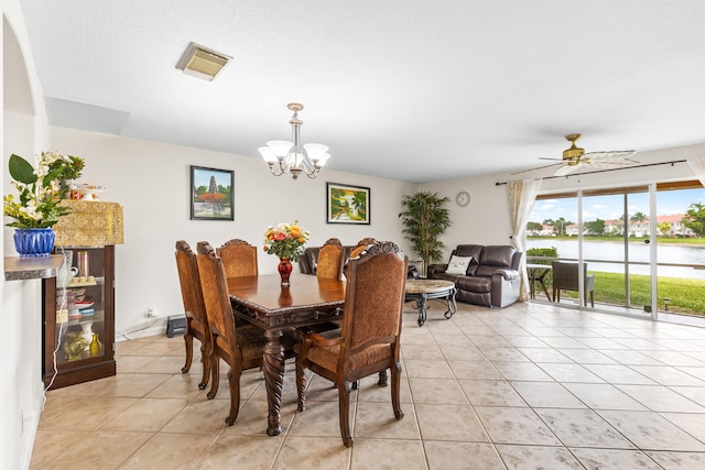 tiled dining area with ceiling fan with notable chandelier and a water view