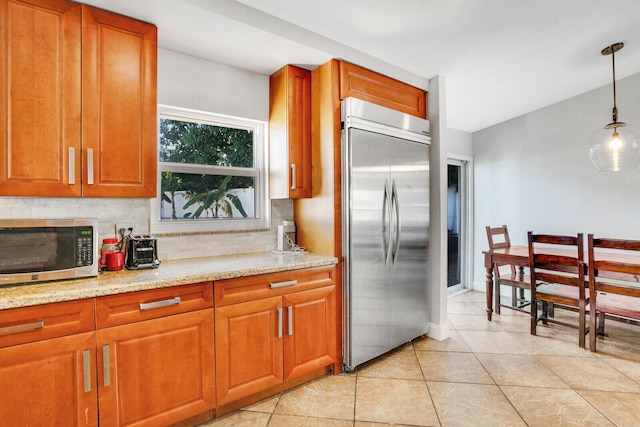 kitchen with stainless steel appliances, light stone counters, decorative light fixtures, decorative backsplash, and light tile patterned floors