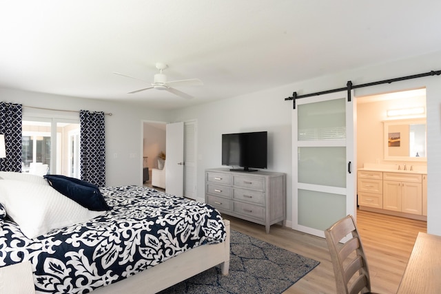 bedroom featuring a barn door, light wood-type flooring, ceiling fan, sink, and ensuite bathroom