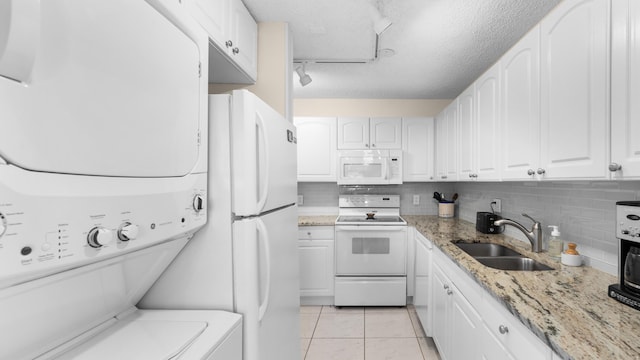 kitchen with light stone countertops, stacked washing maching and dryer, white appliances, sink, and white cabinetry