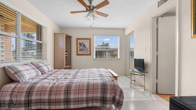 bedroom featuring ceiling fan, light tile patterned floors, and a textured ceiling