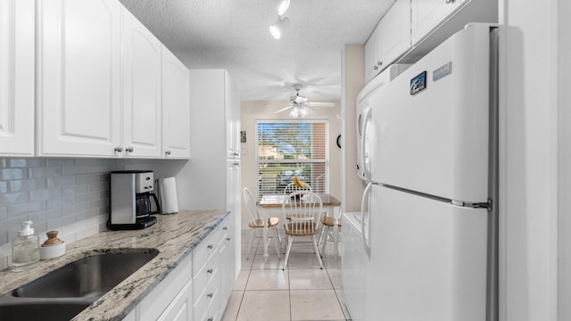 kitchen with white cabinetry, light stone counters, white fridge, a textured ceiling, and decorative backsplash