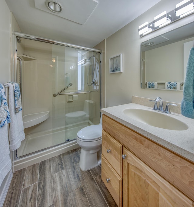 bathroom featuring hardwood / wood-style floors, vanity, a shower with shower door, and toilet