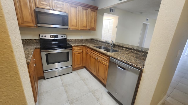 kitchen with kitchen peninsula, appliances with stainless steel finishes, sink, dark stone countertops, and light tile patterned flooring