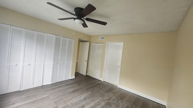 unfurnished bedroom featuring a textured ceiling, light hardwood / wood-style floors, ceiling fan, and multiple closets