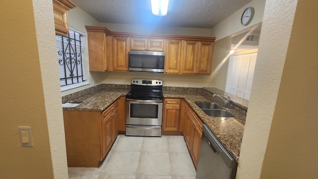 kitchen with appliances with stainless steel finishes, a textured ceiling, sink, dark stone countertops, and light tile patterned flooring