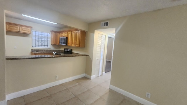 kitchen featuring kitchen peninsula, light tile patterned floors, stainless steel appliances, and dark stone countertops