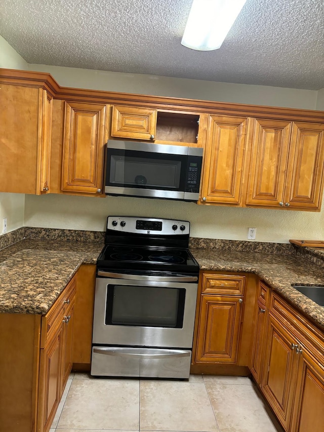 kitchen with light tile patterned floors, a textured ceiling, stainless steel appliances, and dark stone countertops