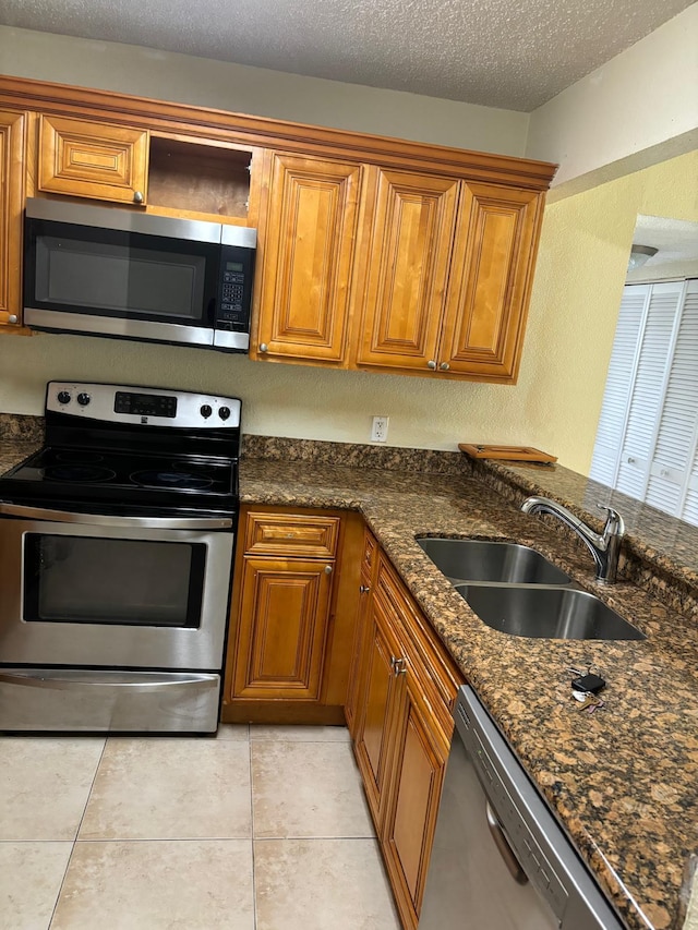 kitchen featuring dark stone counters, a textured ceiling, stainless steel appliances, sink, and light tile patterned floors