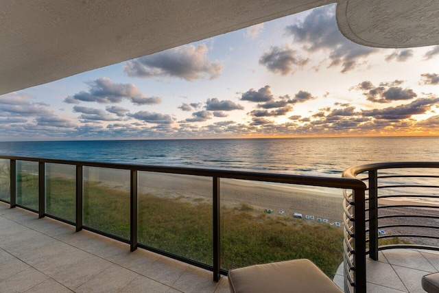 balcony at dusk featuring a beach view and a water view