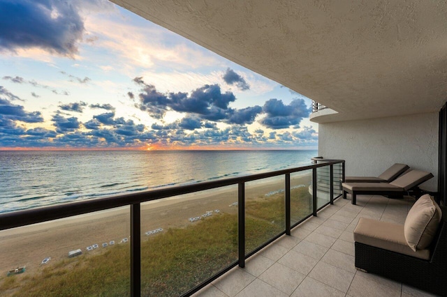 balcony at dusk with a water view and a view of the beach