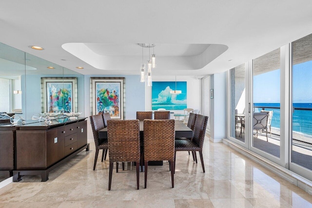 dining room with a water view, an inviting chandelier, a raised ceiling, and expansive windows