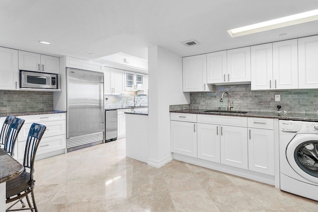 kitchen featuring sink, built in appliances, washer / clothes dryer, and white cabinetry