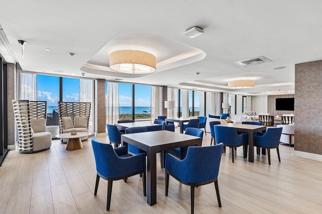 dining area with a wall of windows, light hardwood / wood-style flooring, and a raised ceiling