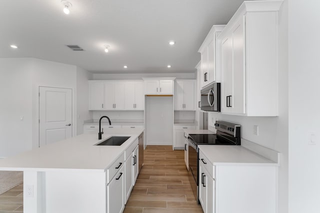 kitchen with appliances with stainless steel finishes, a kitchen island with sink, sink, light hardwood / wood-style floors, and white cabinetry