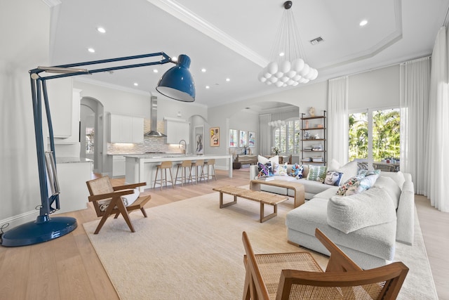 living room with a tray ceiling, sink, light hardwood / wood-style floors, and ornamental molding