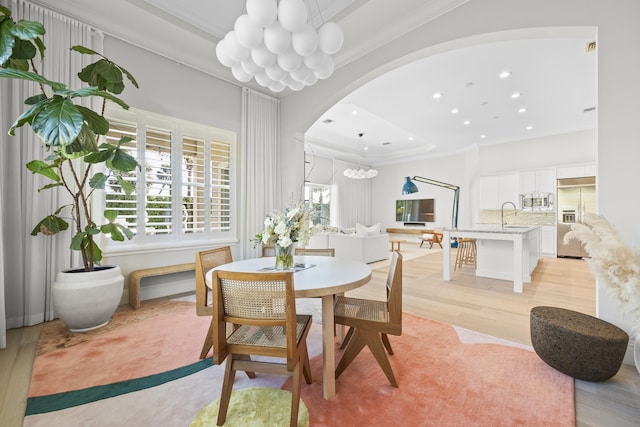 dining space featuring a notable chandelier, light hardwood / wood-style floors, sink, and crown molding