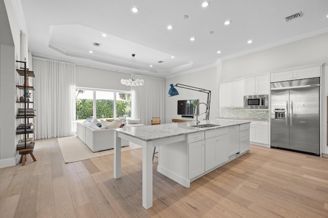 kitchen featuring sink, built in appliances, decorative light fixtures, a kitchen island with sink, and white cabinets