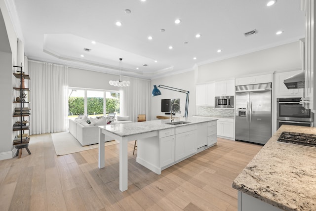 kitchen featuring white cabinets, built in appliances, a kitchen island with sink, and sink