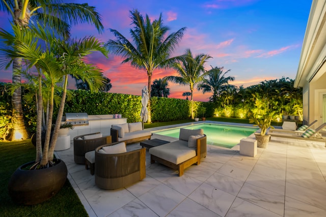 patio terrace at dusk featuring an outdoor kitchen, a grill, and a fenced in pool