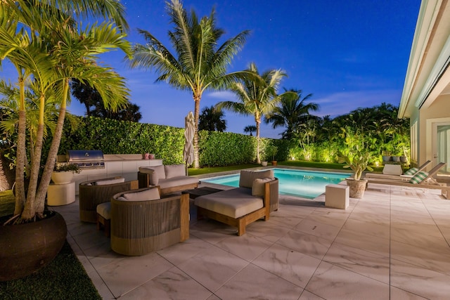 pool at dusk with a patio area, area for grilling, and an outdoor kitchen