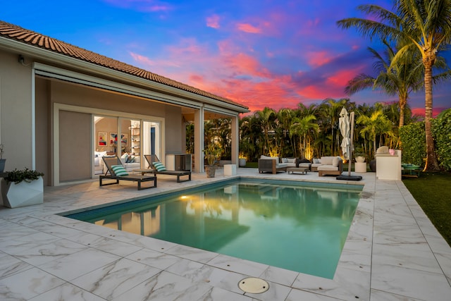 pool at dusk with an outdoor living space and a patio area