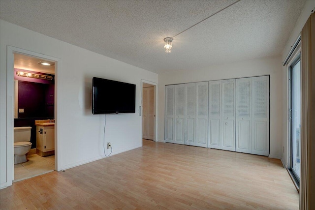 unfurnished bedroom featuring a textured ceiling, light hardwood / wood-style flooring, ensuite bath, and multiple windows