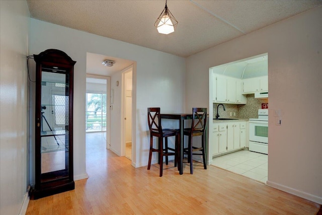 kitchen featuring sink, light hardwood / wood-style flooring, white electric range, white cabinetry, and hanging light fixtures