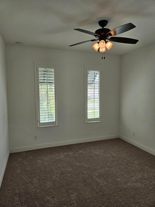 empty room featuring dark carpet, a wealth of natural light, and baseboards