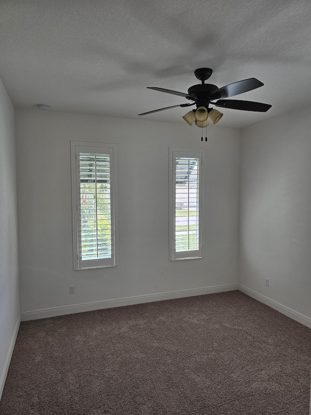 unfurnished room with dark colored carpet, plenty of natural light, a textured ceiling, and baseboards