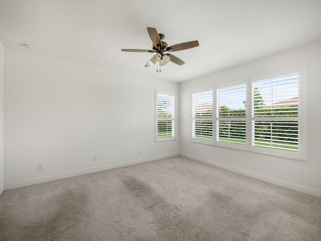 spare room featuring a ceiling fan, light colored carpet, and baseboards